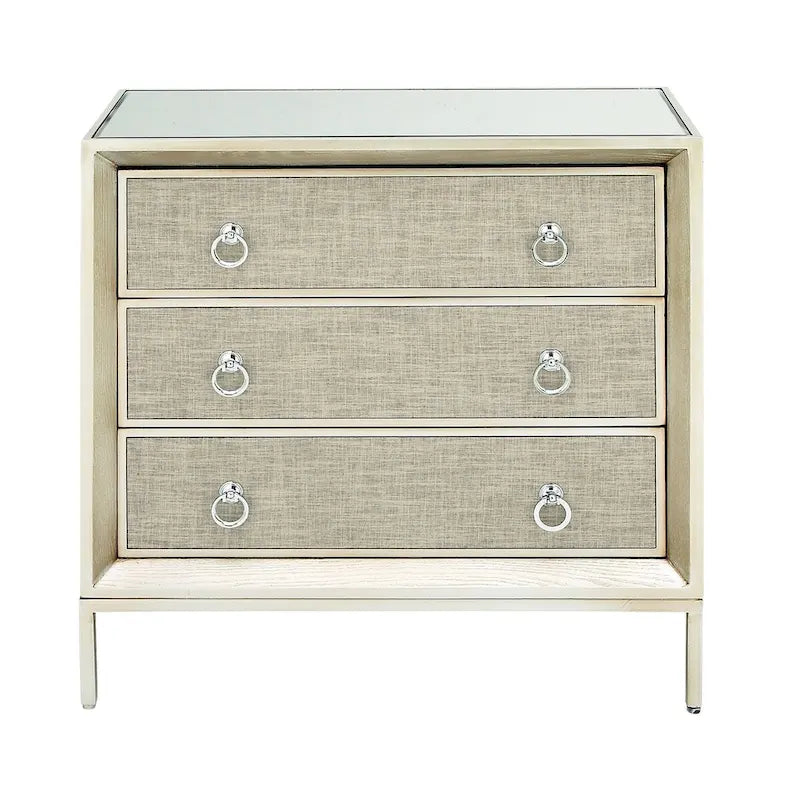 Commode en bois à trois tiroirs avec finition capitonnée, plateau miroir et poignées anneaux.