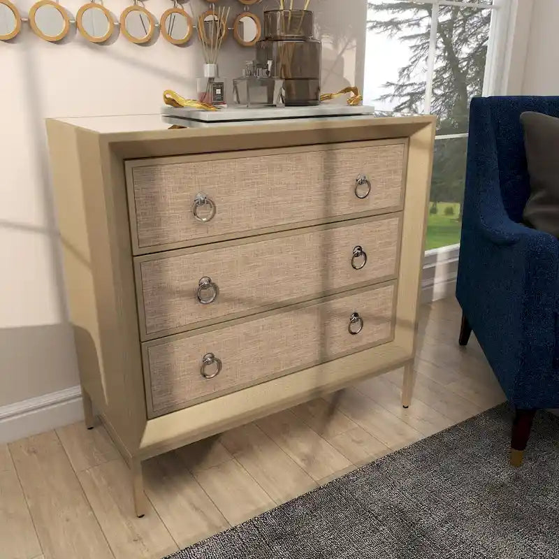 Commode en bois à trois tiroirs avec finition capitonnée, plateau miroir et poignées anneaux.