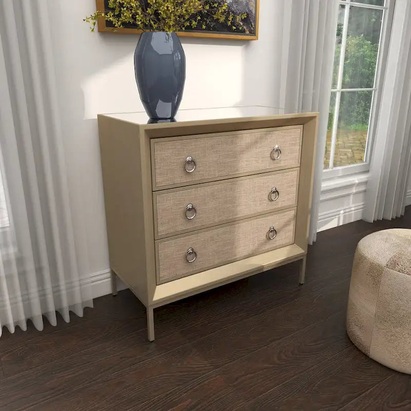 Commode en bois à trois tiroirs avec finition capitonnée, plateau miroir et poignées anneaux.