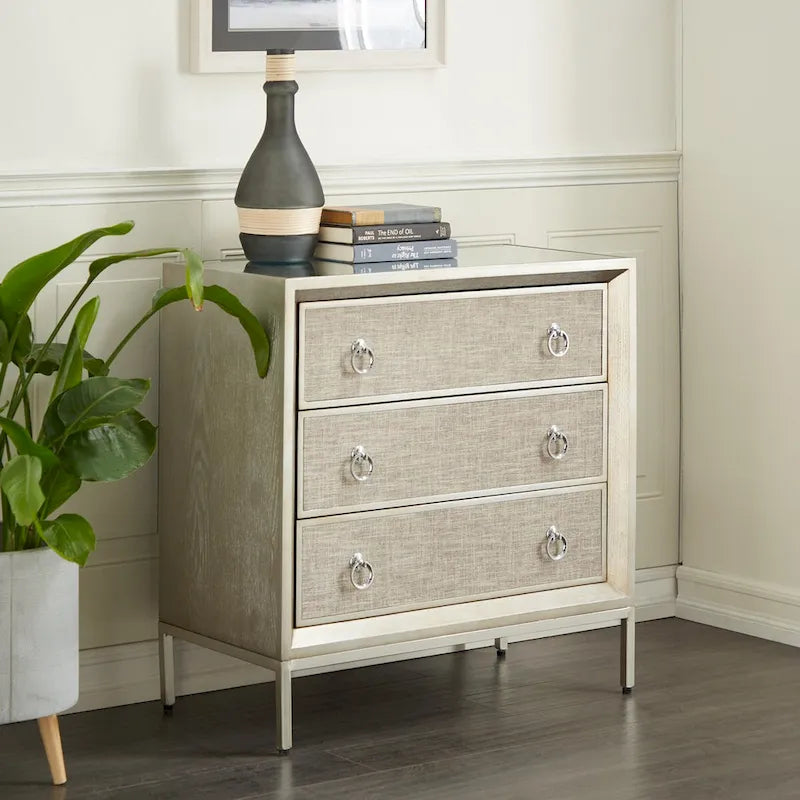 Commode en bois à trois tiroirs avec finition capitonnée, plateau miroir et poignées anneaux.