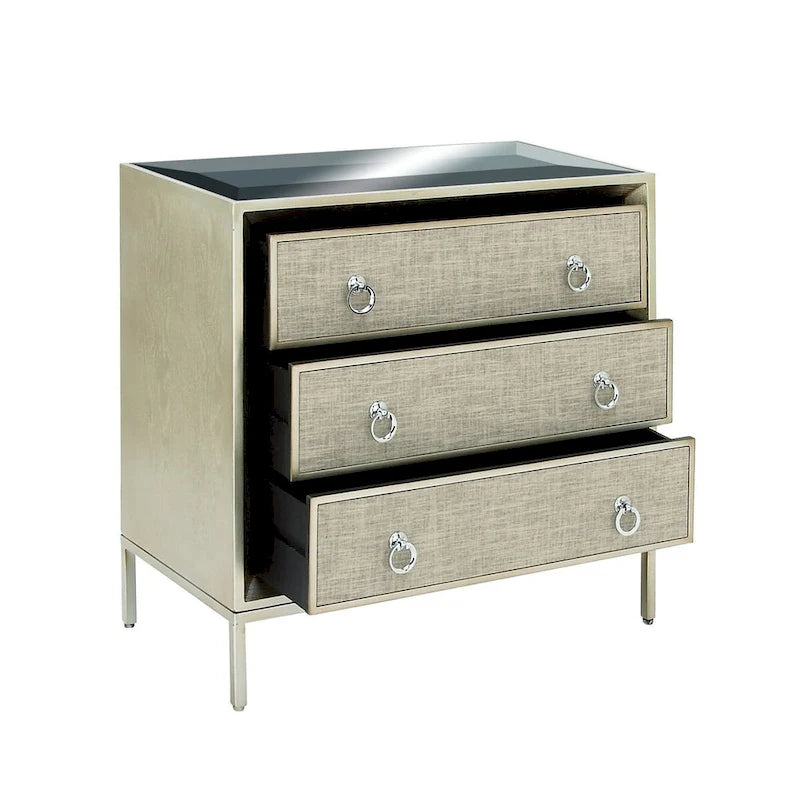 Commode en bois à trois tiroirs avec finition capitonnée, plateau miroir et poignées anneaux.