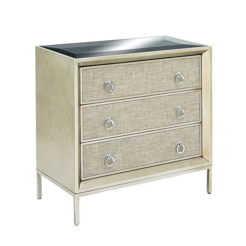 Commode en bois à trois tiroirs avec finition capitonnée, plateau miroir et poignées anneaux.